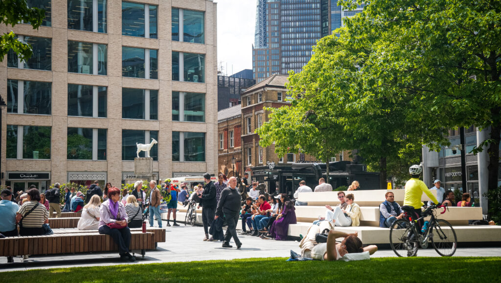 Bishopsgate Plaza pocket park – Locals lounging on benches and cyclists passing in green public square near Spitalfields, East London