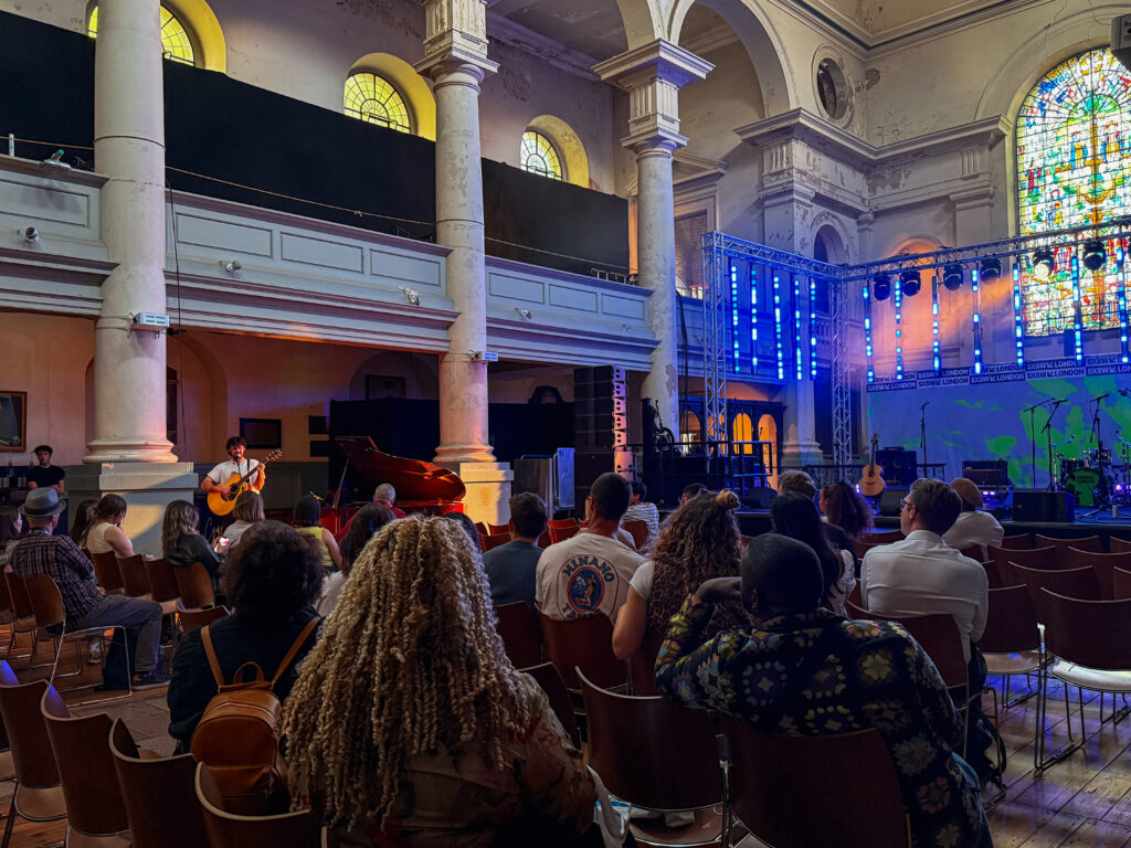 St Leonard’s church session – Audience seated inside historic Shoreditch church watching acoustic set on blue‑lit SXSW London stage.